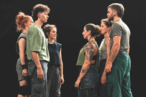 6 mensen in groene kleding staan tegenover elkaar op een podium