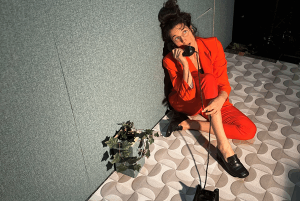 vrouw in rood pak zit in een hoek op de grond met een draaischijftelefoon in haar hand