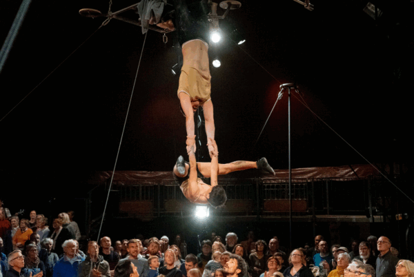 2 mensen die aan een trapeze hangen in een circustent