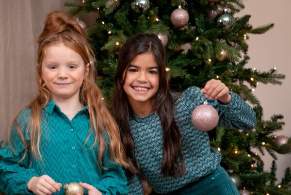 2 meisjes voor een kerstboom en met een kerstbal in de hand